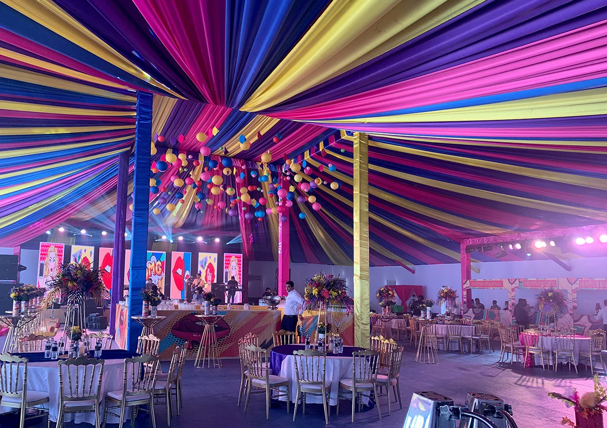 wedding marquee UAE - Vibrant wedding arch tent with colorful draped ceiling in pink, blue, and yellow. Festive hanging balloons, elegant tables, and illuminated stage create a cheerful atmosphere. - Wedding Marquee - Alfares International Tents
